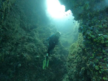 A diver exploring a sunlit underwater cave