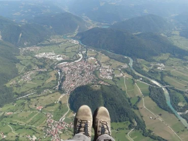 A paraglider's-eye view of boots hanging over a river valley and town far below